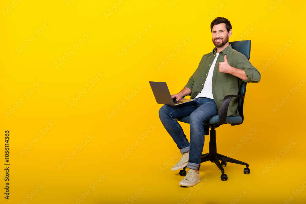 Full length portrait of nice young man sit chair netbook thumb up wear shirt isolated on yellow color background Full length portrait of nice young man sit chair netbook thumb up wear shirt isolated on yellow color background