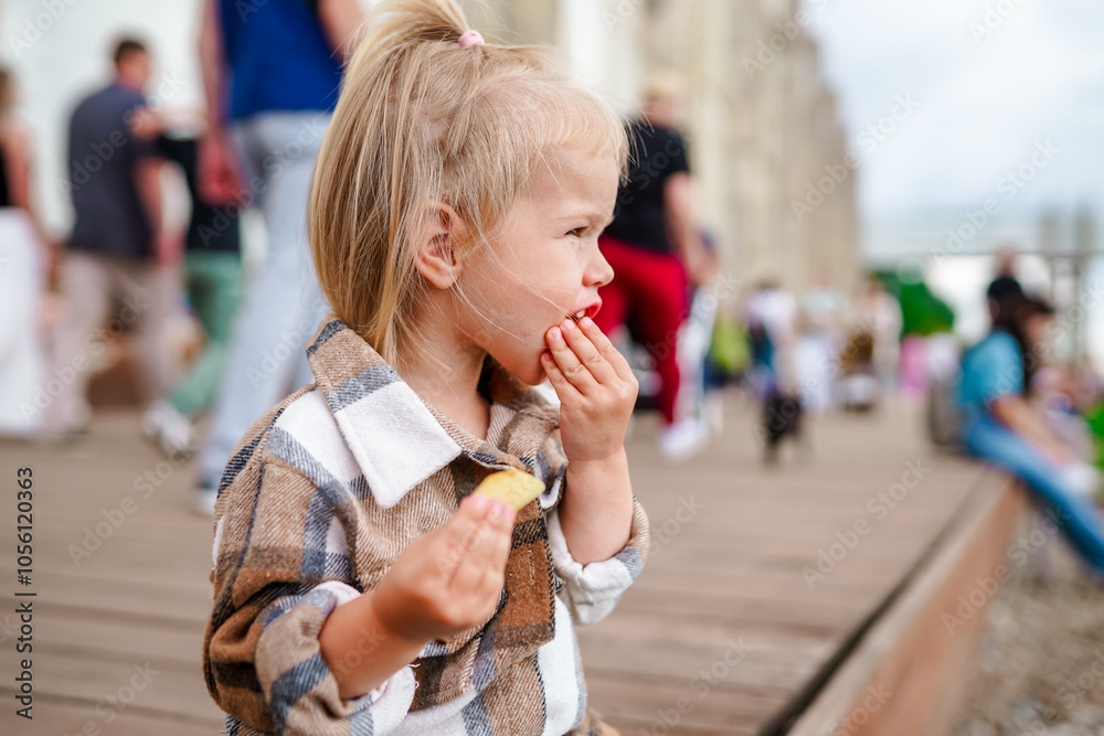 Cute stylish toddler child girl sits on a wooden platform in a crowded street in summer. Saint Petersburg, Russia - 10 July 2024 Cute stylish toddler child girl sits on a wooden platform in a crowded street in summer. Saint Petersburg, Russia - 10 July 2024