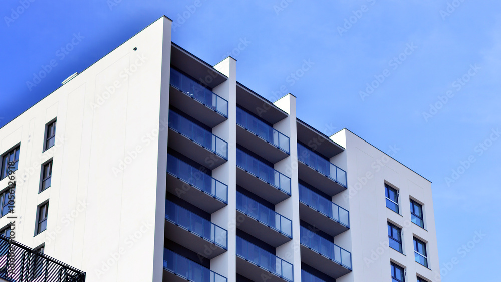 Fototapeta premium Modern high-rise apartment building in white, stand tall against a blue sky, exemplifying innovative urban architecture with sleek, angular designs.