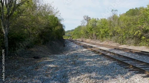 Low UAV dolly toward double railroad tracks past shopping cart, then dolly forward.