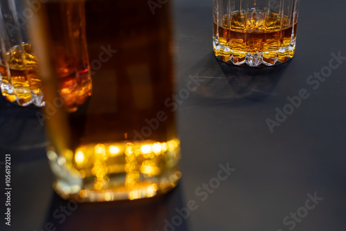 Glass with whisky close-up on dark background and whisky bottle on blurred foreground photo