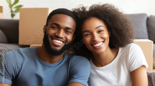 A young couple smiles happily while sitting in their new home surrounded by moving boxes