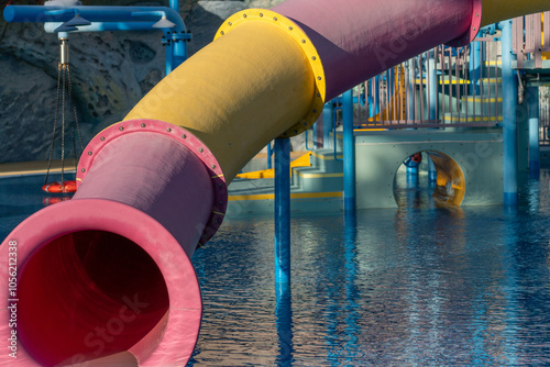 Waterpark Slide Pool Fun - Close-up of a pink and yellow water slide at a waterpark. The slide is situated above a blue pool. photo