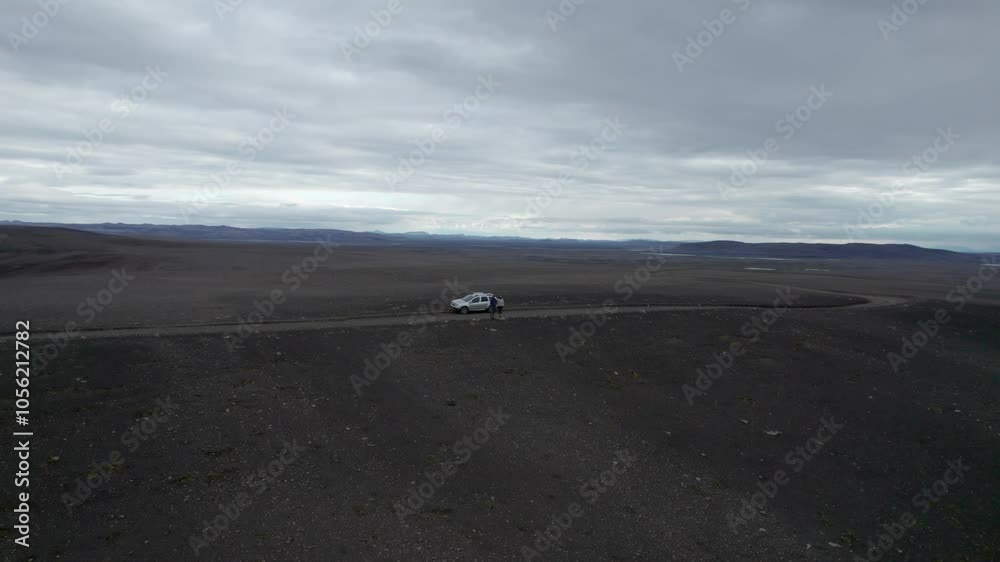 A couple of people stand on the side of a road in a remote Icelandic desert, surrounded by vast, barren landscapes. The empty road stretches through the rugged terrain under an open sky. A couple of people stand on the side of a road in a remote Icelandic desert, surrounded by vast, barren landscapes. The empty road stretches through the rugged terrain under an open sky.