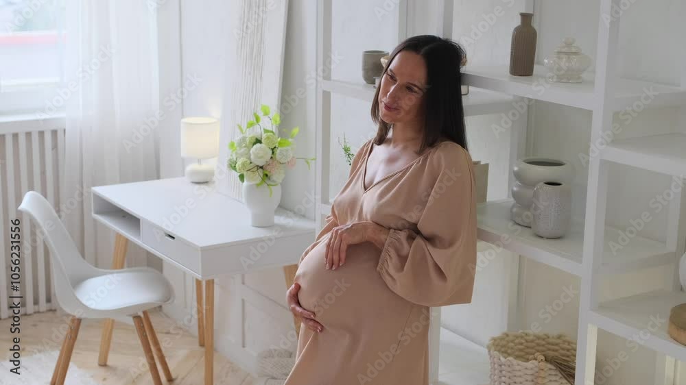 Joyful pregnant Caucasian middle aged woman tenderly stroke a baby bump at home living room. Planning and preparation to future motherhood. Joyful pregnant Caucasian middle aged woman tenderly stroke a baby bump at home living room. Planning and preparation to future motherhood.