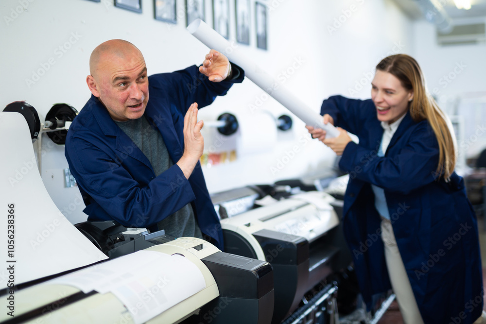 Fototapeta premium Positive printing office workers in uniform fighting with rolled paper during break just for fun.