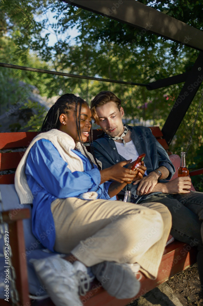 Woman sharing smart phone with male friend while sitting on bench at party Woman sharing smart phone with male friend while sitting on bench at party