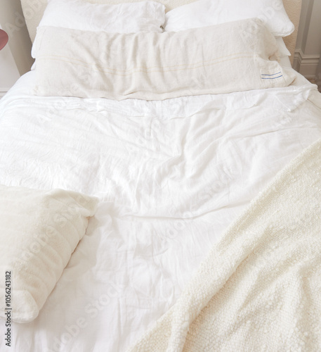 A cozy and inviting bed with soft, white linens, a textured blanket, and plush pillows arranged in a minimal and neutral-toned bedroom. The natural light highlights the simplicity and comfort of the s photo