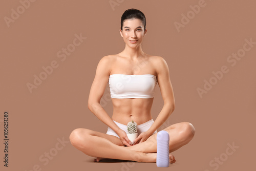 Beautiful young happy woman with liposoluble wax cartridge and cactus sitting on brown background. Depilation concept photo