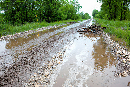 a country road submerged in muddy floodwaters, strewn with broken branches and stones