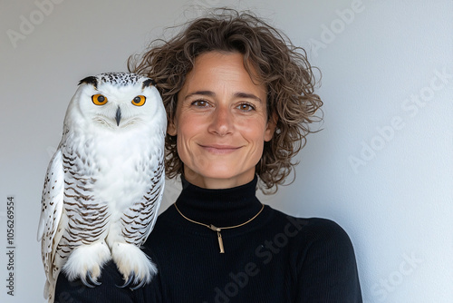 a serene woman and her snowy owl, posed in front of a minimal background
 photo