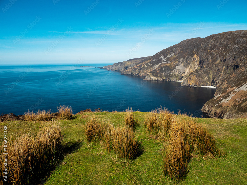 Obraz premium Stunning picturesque view on Slieve league cliffs, county Donegal, Ireland. Warm sunny day. Irish landscape scene. Blue cloudy sky and ocean surface, rough and tall cliffs.