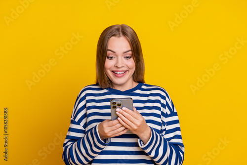 Photo of excited adorable cute woman wear striped stylish clothes read phone isolated on yellow color background