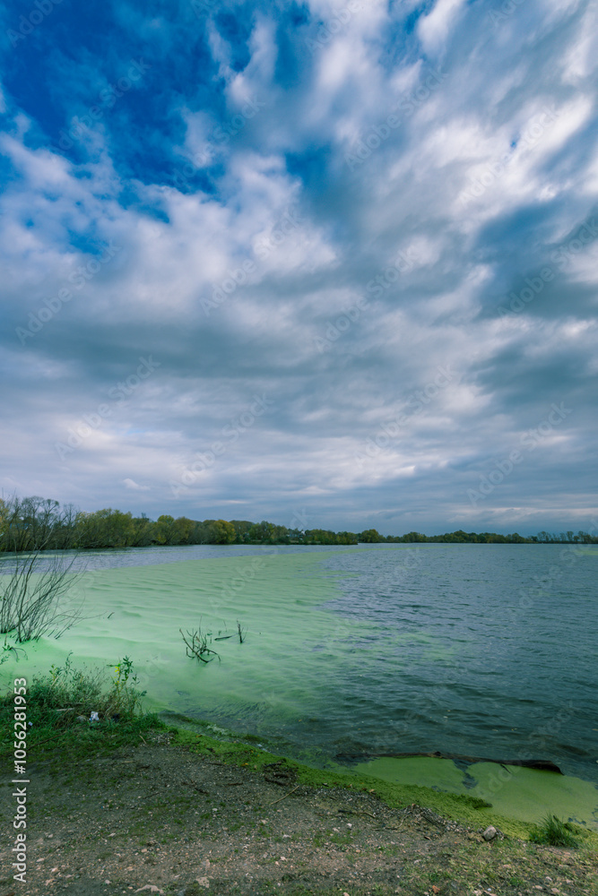 Fototapeta premium A lake with green water and a cloudy sky in the background