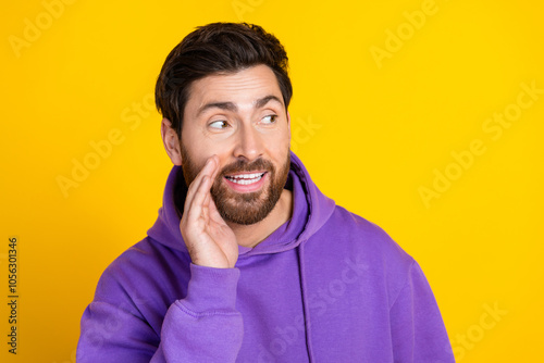 Portrait of funky man with stylish bristle dressed purple hoodie hold hand on mouth look empty space isolated on yellow color background