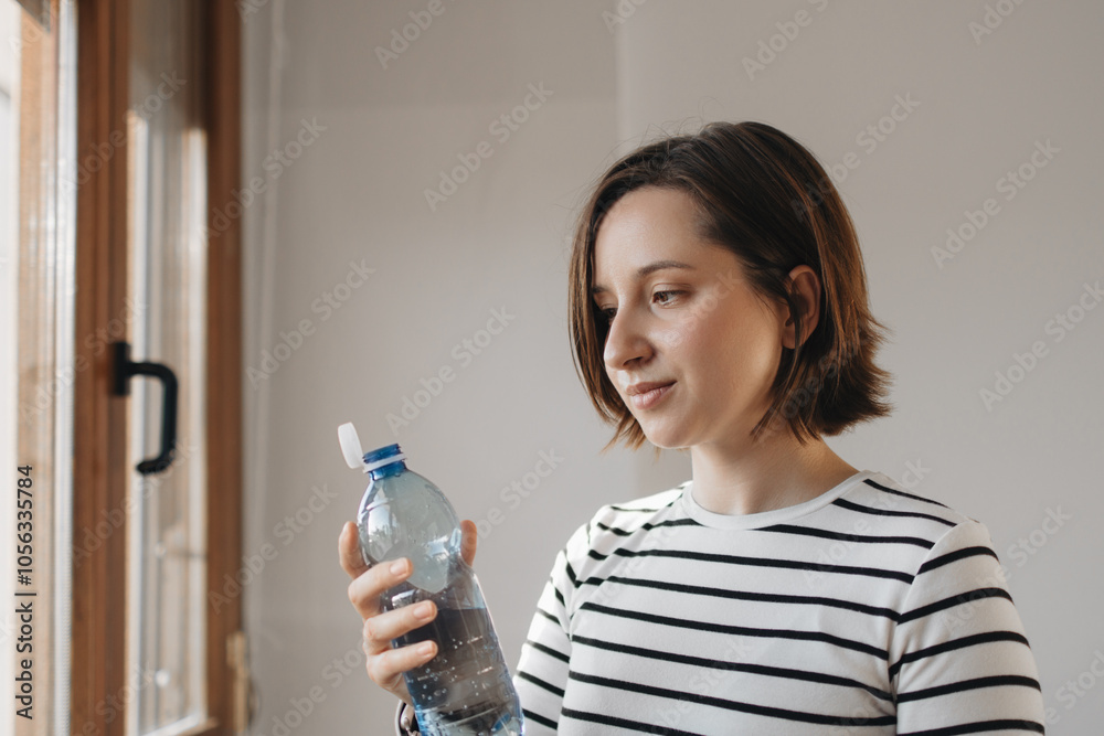 Young Woman Holding And Looking At Reusable Water Bottle With New Tethered Caps On Plastic Water Bottles, Promoting Sustainability And Hydration. New Eu Regulation Young Woman Holding And Looking At Reusable Water Bottle With New Tethered Caps On Plastic Water Bottles, Promoting Sustainability And Hydration. New Eu Regulation