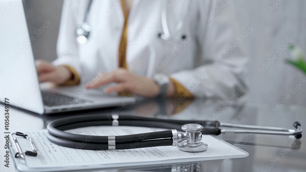 © volha_r - Stethoscope and clipboard with medication history records are on a glass desk behind a physician using a laptop computer. Medicine concept © volha_r - Stethoscope and clipboard with medication history records are on a glass desk behind a physician using a laptop computer. Medicine concept