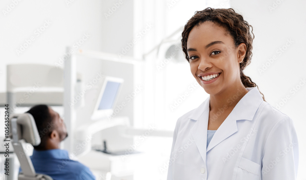 Attractive black woman dentist smiling at camera over guy patient waiting for treatment, clinic interior, copy space Attractive black woman dentist smiling at camera over guy patient waiting for treatment, clinic interior, copy space