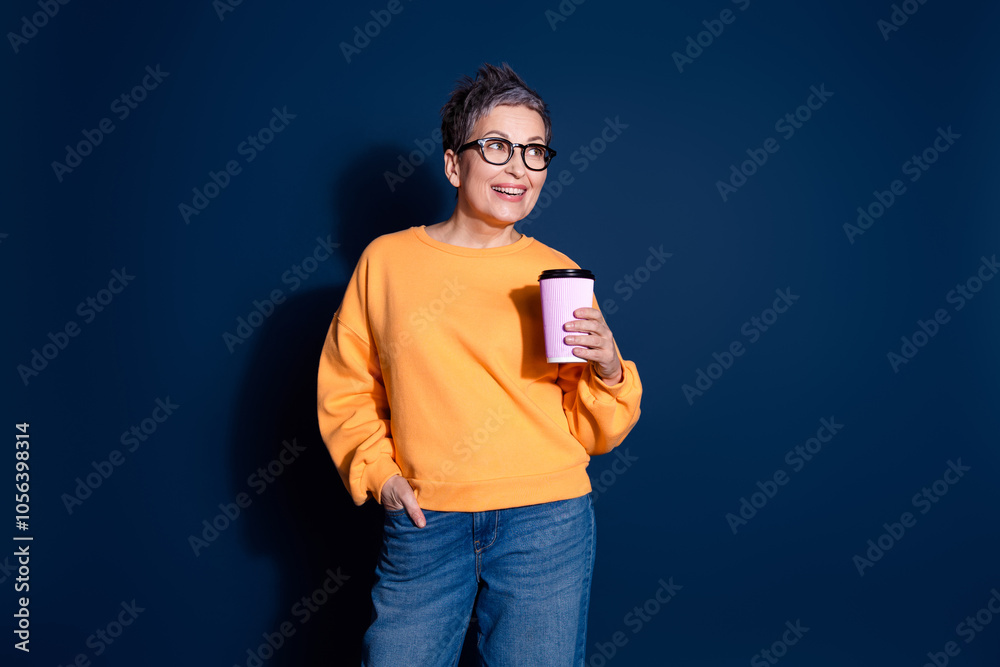 Photo of lovely pensioner lady look empty space hold coffee paper cup dressed stylish yellow garment isolated on dark blue color background