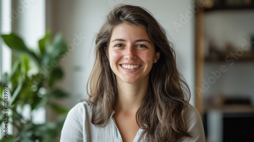 woman smiling in bright apartment, surrounded by greenery, exuding warmth and positivity. Her relaxed demeanor creates welcoming atmosphere