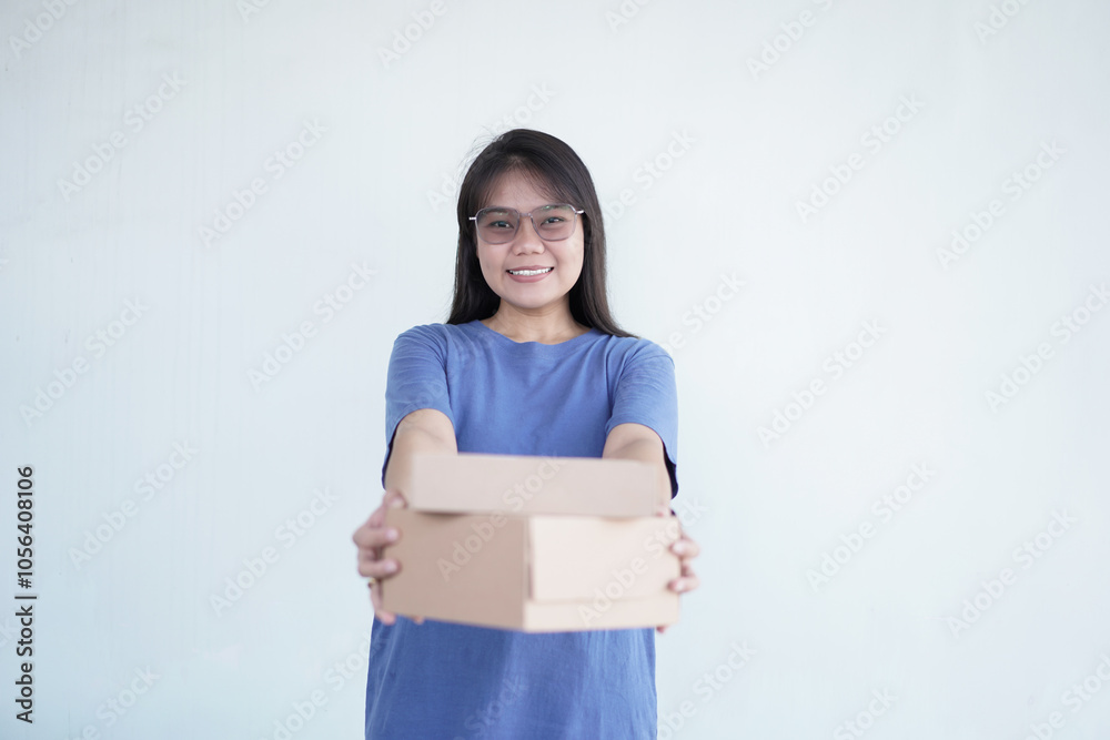Beautiful Asian woman smiles warmly while holding a package box against a bright white background Beautiful Asian woman smiles warmly while holding a package box against a bright white background