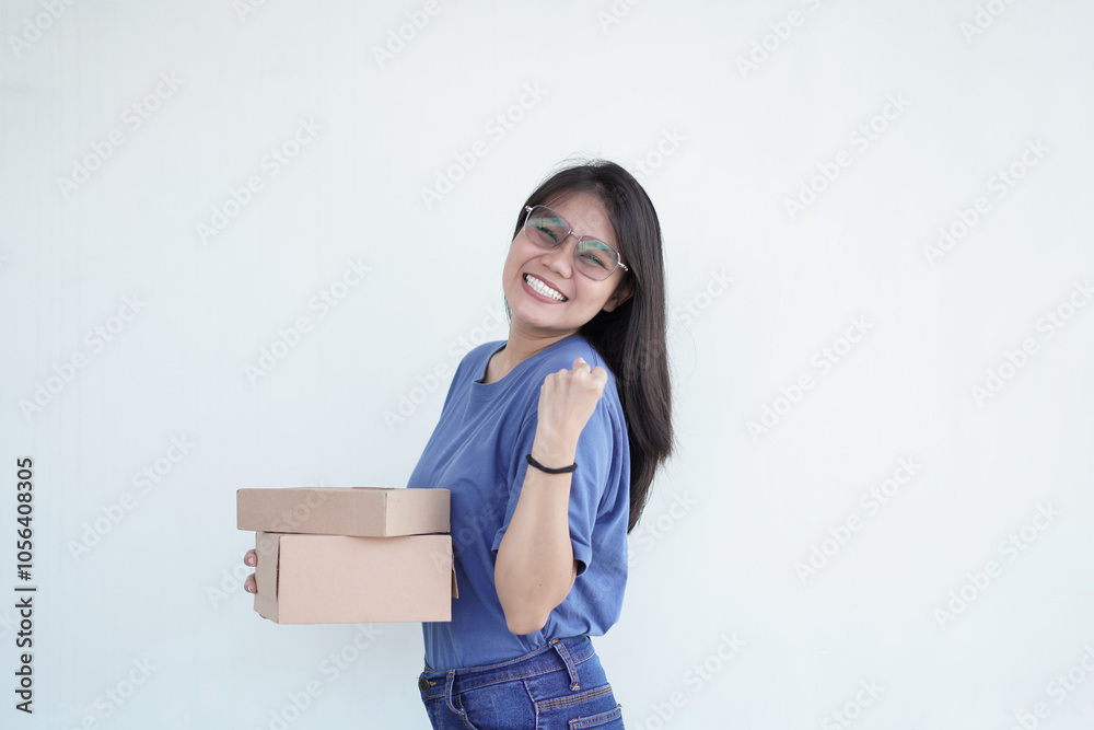 Beautiful Asian woman smiles happily, making a 'yes' gesture while holding a package box against a white background Beautiful Asian woman smiles happily, making a 'yes' gesture while holding a package box against a white background