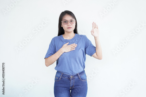 Beautiful Asian woman places her hand on her chest, making a sincere gesture of an oath or promise against a white background