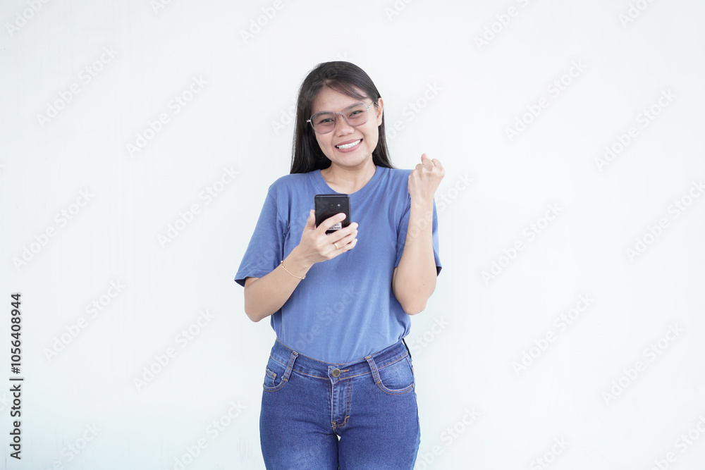Beautiful Asian woman smiles joyfully, celebrating with a 'yes' gesture while using her smartphone against a white background Beautiful Asian woman smiles joyfully, celebrating with a 'yes' gesture while using her smartphone against a white background
