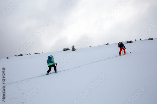 Two skiers ascend a pristine snow-covered slope under overcast skies