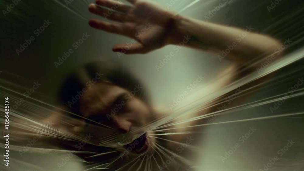 Suffocating man scratching tightly stretched plastic wrap, with face pressed against surface and mouth wide open, trying to escape trap
