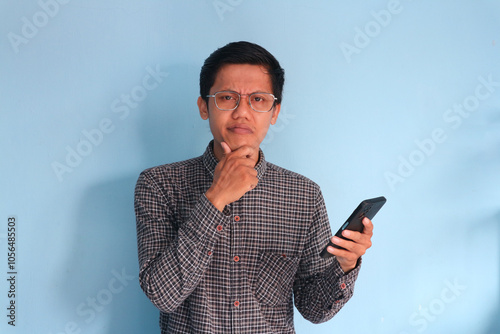 Young asian man showing confused expression while holding mobile phone photo