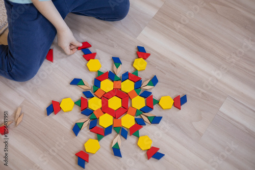 A small white-skinned European boy lays out a mandala pattern on the floor from geometric figures