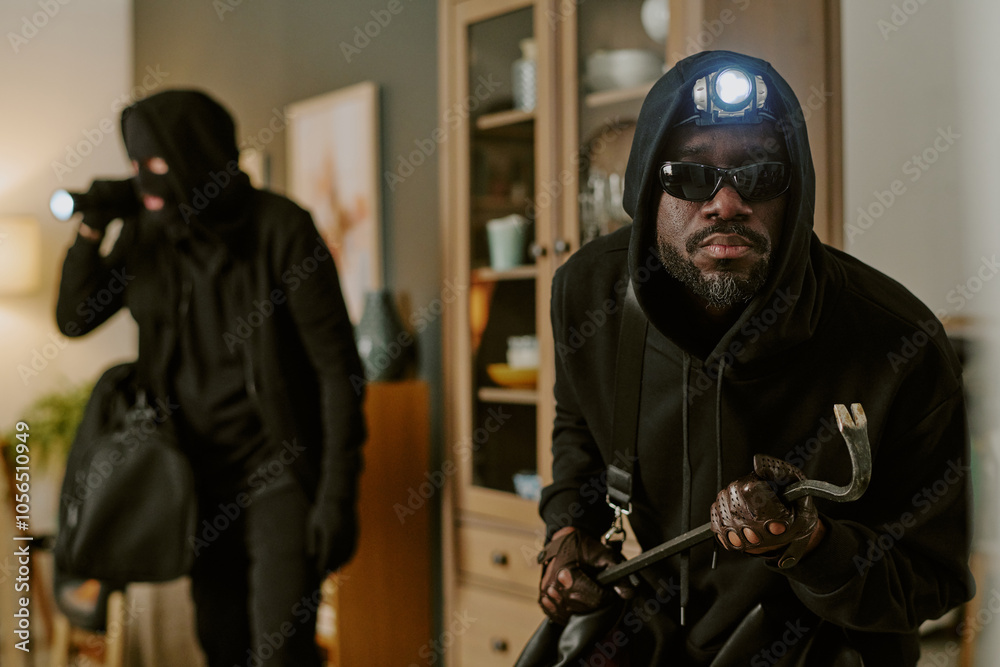 Medium close up of African American thieve with headlamp and crowbar in hands looking at camera during trespassing Medium close up of African American thieve with headlamp and crowbar in hands looking at camera during trespassing