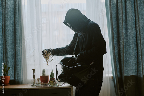 Side view shot of unrecognizable thief grabbing sparkling jewelry from glass box to put them into bag photo