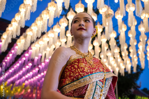 Portrait young pretty woman in traditional dress standing under hanging paper lanterns during Loi Kratong festival in Lamphun, Thailand