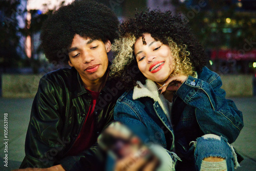 Couple of Latino friends with braces and afro hair enjoying a day at dusk, taking selfies with their cellphone and showing their braces to their friends. Lots of joy, laughter and friendship.