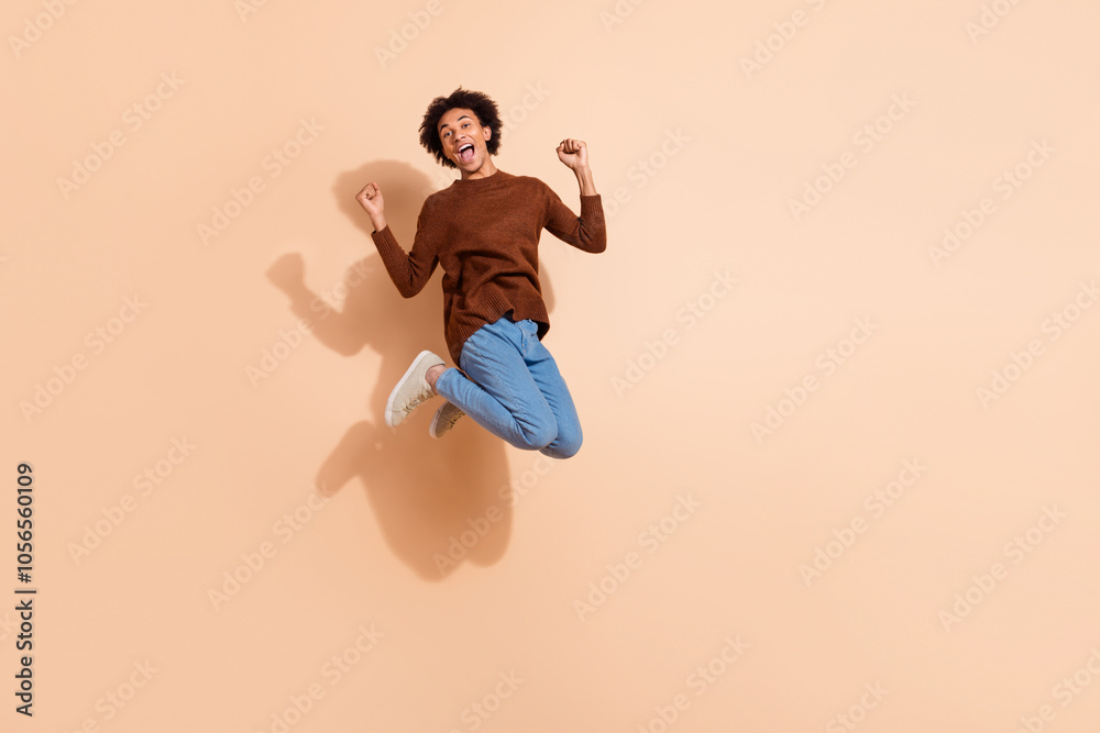 Joyful african american young man in casual outfit jump against beige background, expressing excitement energy for advertising promotions Joyful african american young man in casual outfit jump against beige background, expressing excitement energy for advertising promotions