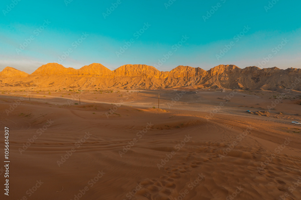 Fototapeta premium layer of desert mountains during winter in the deep desert with golden sand dunes. blue sky in the horizon foot markings in sand during golden hour adventurous desert safari