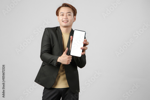 portrait of happy asian businessman wearing suit holding mobile phone and showing blank screen giving thumb up gesture on isolated background.