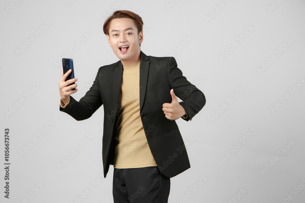 portrait of happy asian businessman wearing suit holding mobile phone giving thumb up gesture on isolated background. portrait of happy asian businessman wearing suit holding mobile phone giving thumb up gesture on isolated background.