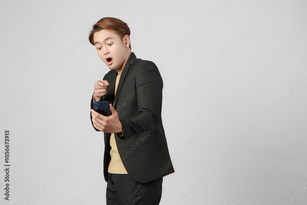 portrait of shocked surprised asian businessman wearing suit holding mobile phone on isolated background portrait of shocked surprised asian businessman wearing suit holding mobile phone on isolated background