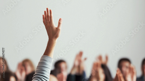 A hand is raised among a blurred audience, symbolizing participation, question-asking, or engagement in a seminar or educational setting.