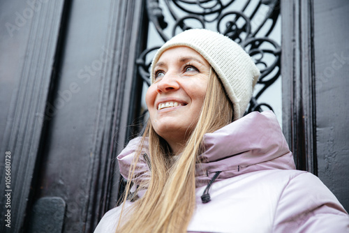 Woman in winter jacket and hat smiling near ornate background outdoors