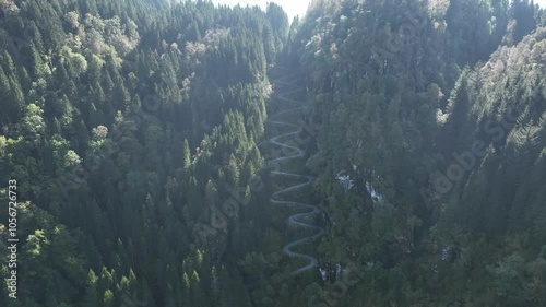 High altitude aerial over Kossdalen valley, revealing lush forest and winding hairpin road turns in sunlight photo