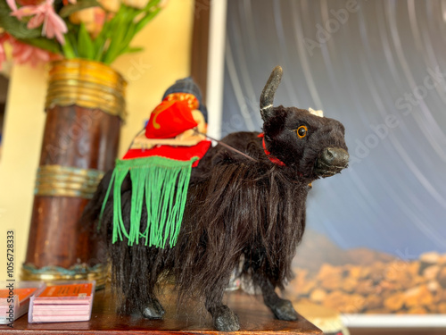 A stuffed yak with a red and green saddle is sitting on a wooden table photo