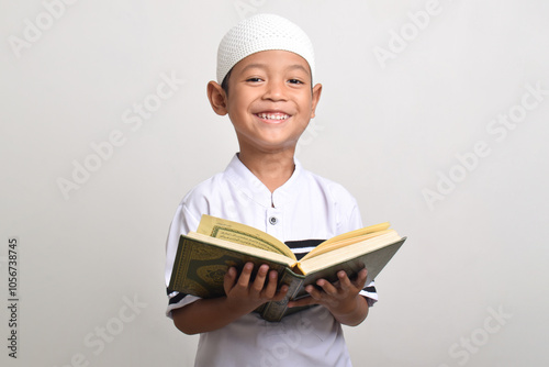 Portrait of smiling Muslim boy reading Quran isolated on white background. Ramadan and Eid Mubarak concept photo