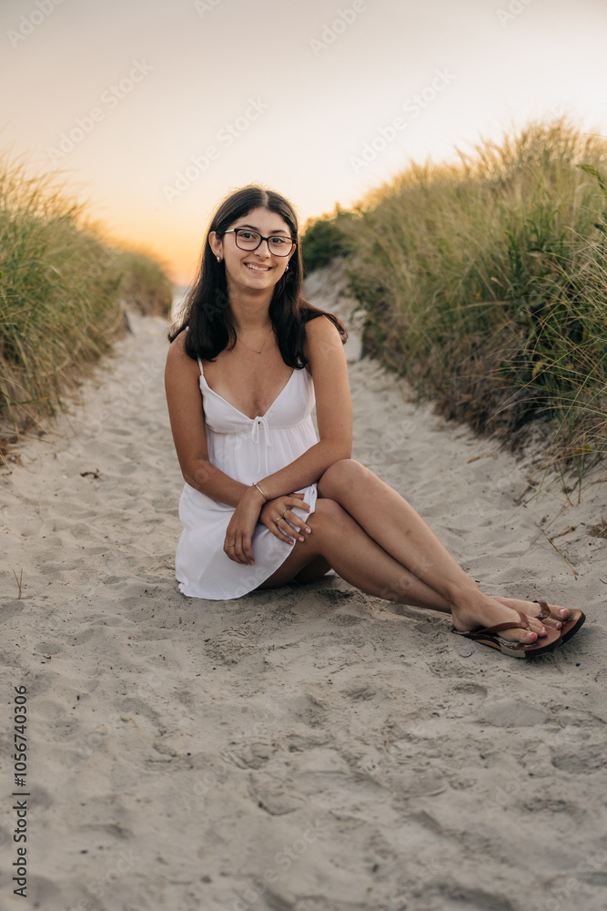 Woman sitting on a sandy path at sunset, smiling in a white dress Woman sitting on a sandy path at sunset, smiling in a white dress