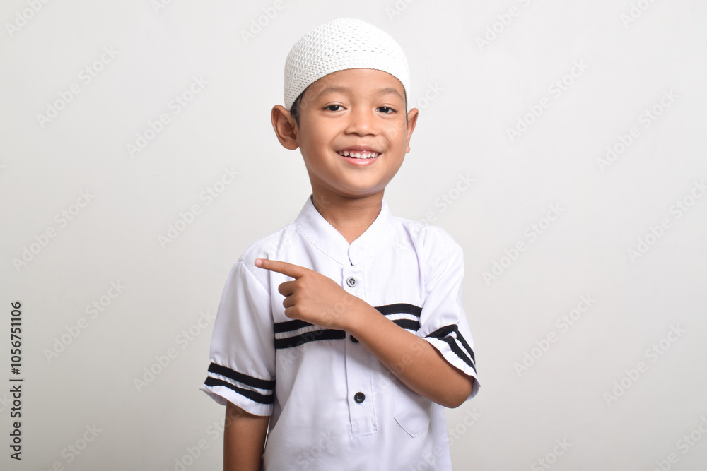 Portrait of a cheerful Asian Muslim boy with finger pointing to the side isolated on white background. Finger pointing to copy space Portrait of a cheerful Asian Muslim boy with finger pointing to the side isolated on white background. Finger pointing to copy space