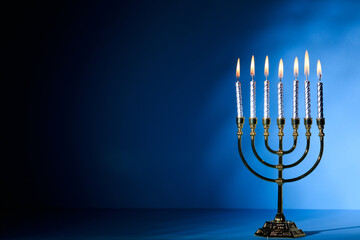 Hanukkah menorah with glowing candles on blue backdrop, symbolizing Jewish festival of lights