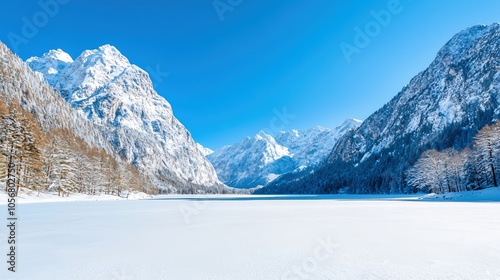 A breathtaking winter mountain vista featuring majestic peaks blanketed in deep snow under a clear blue sky. The foreground showcases a tranquil frozen lake reflecting the surrounding landscape. This